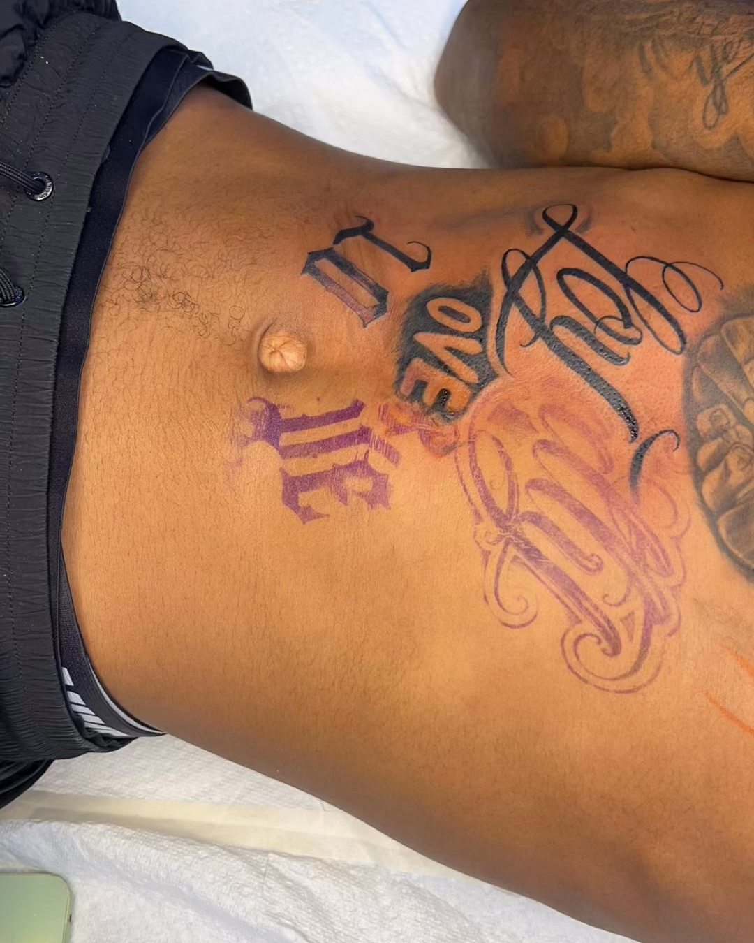 Lettering tattoo across a torso with purple stencil lines still visible