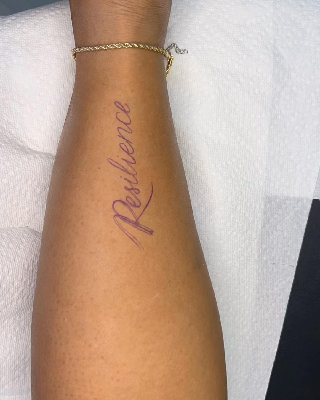 Fine script word tattooed vertically down a forearm