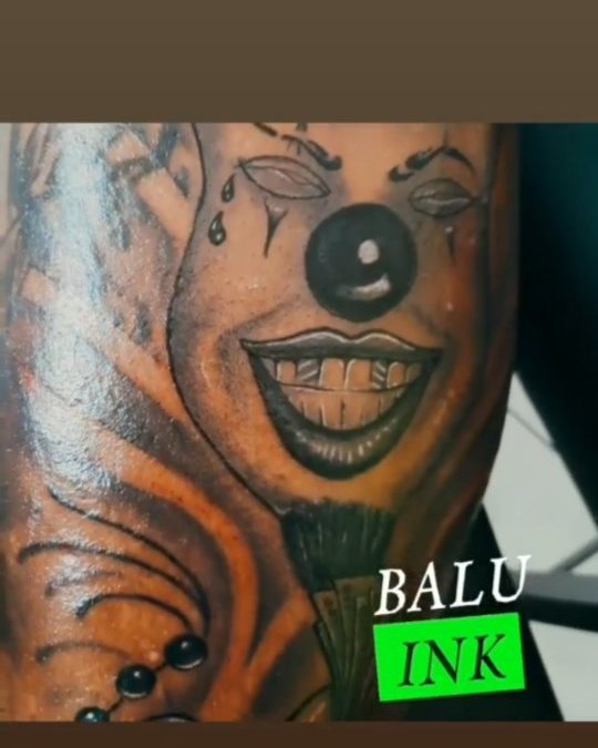 Colour portrait tattoo of a clown face with lettering on a forearm