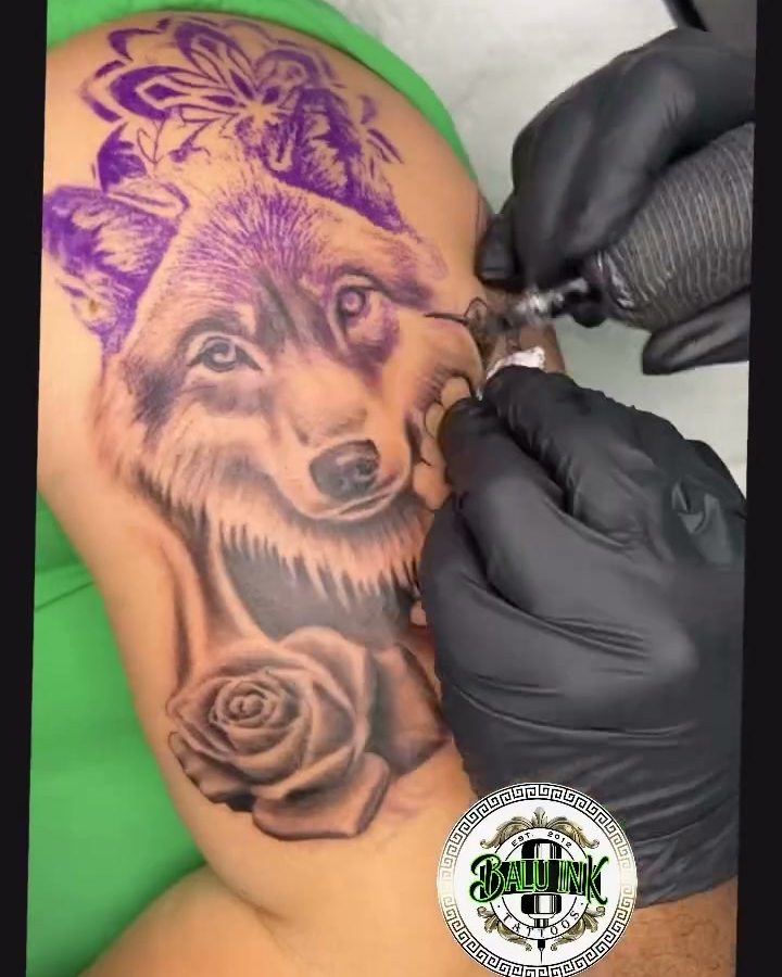Wolf tattoo in progress on a leg with a purple stencil and a gloved hand holding a tattoo machine